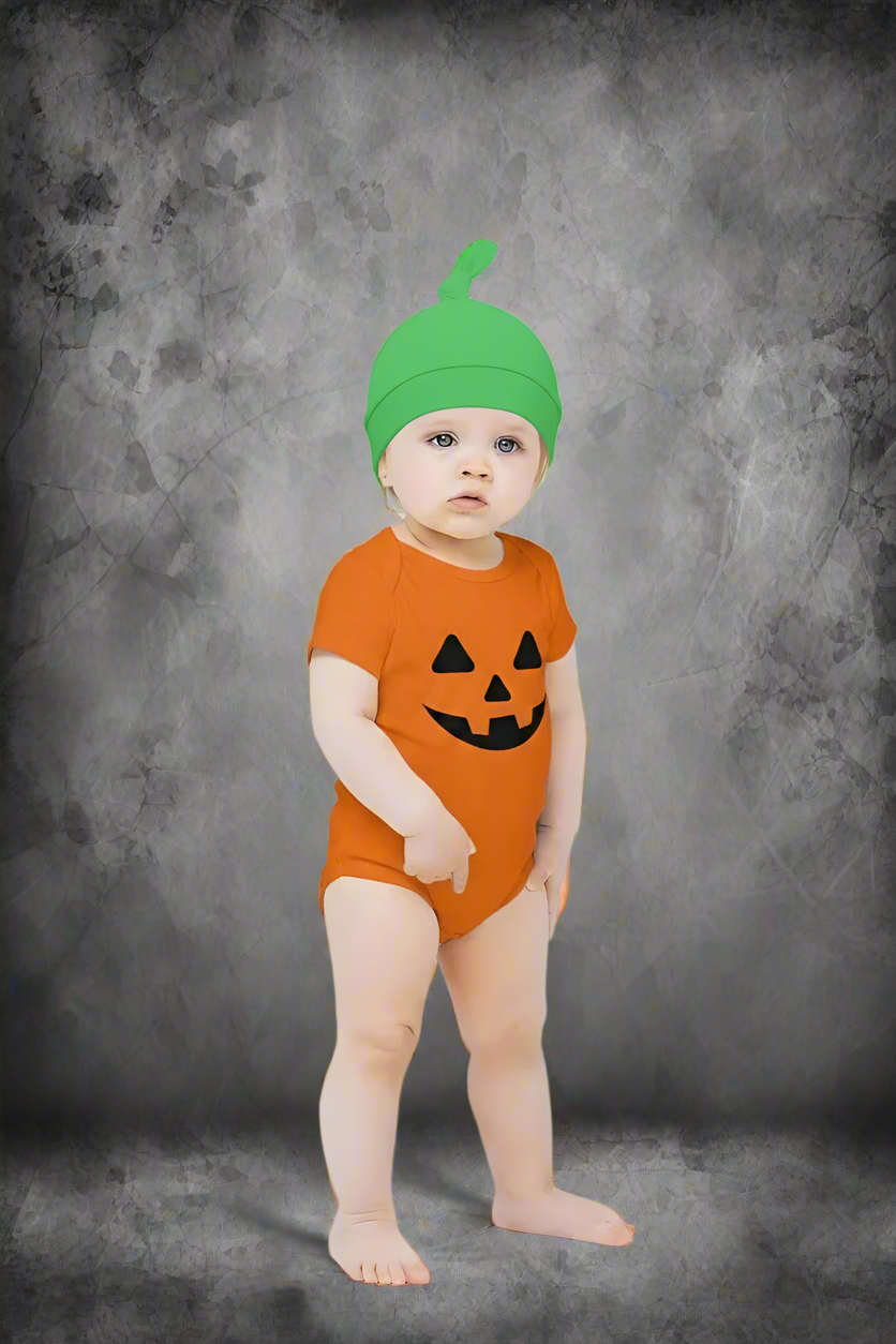Baby wearing an orange pumpkin costume with a green hat on a light gray background